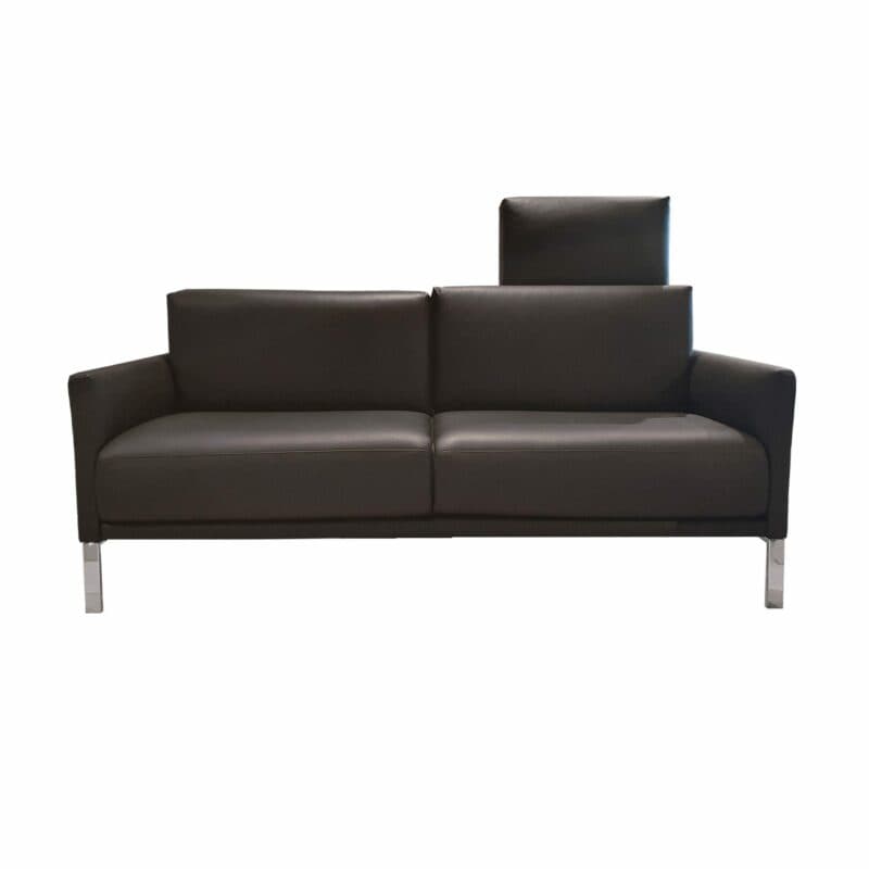 Rolf Benz „Cara” Sofabank mit Bezug 38.110 verkehrsschwarz sowie einem Spangengestell in Glanzchrom und einer Kopfstütze links in frontaler Ansicht.