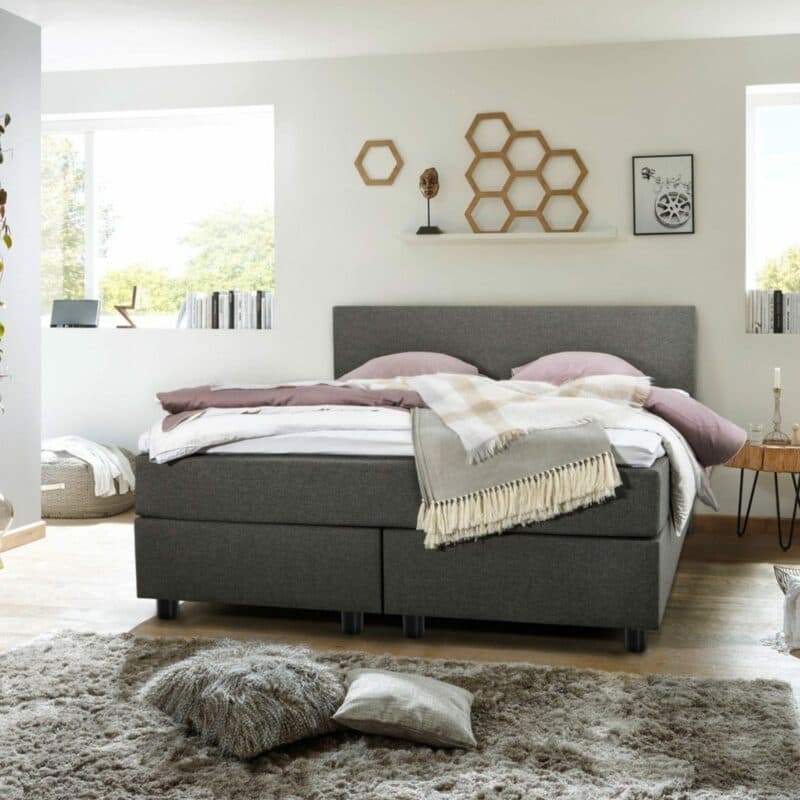 Akador Night Akkala Boxspringbett mit Textilbezug in Grau und Füßen aus Holz in Schwarz als Wohnbeispiel.