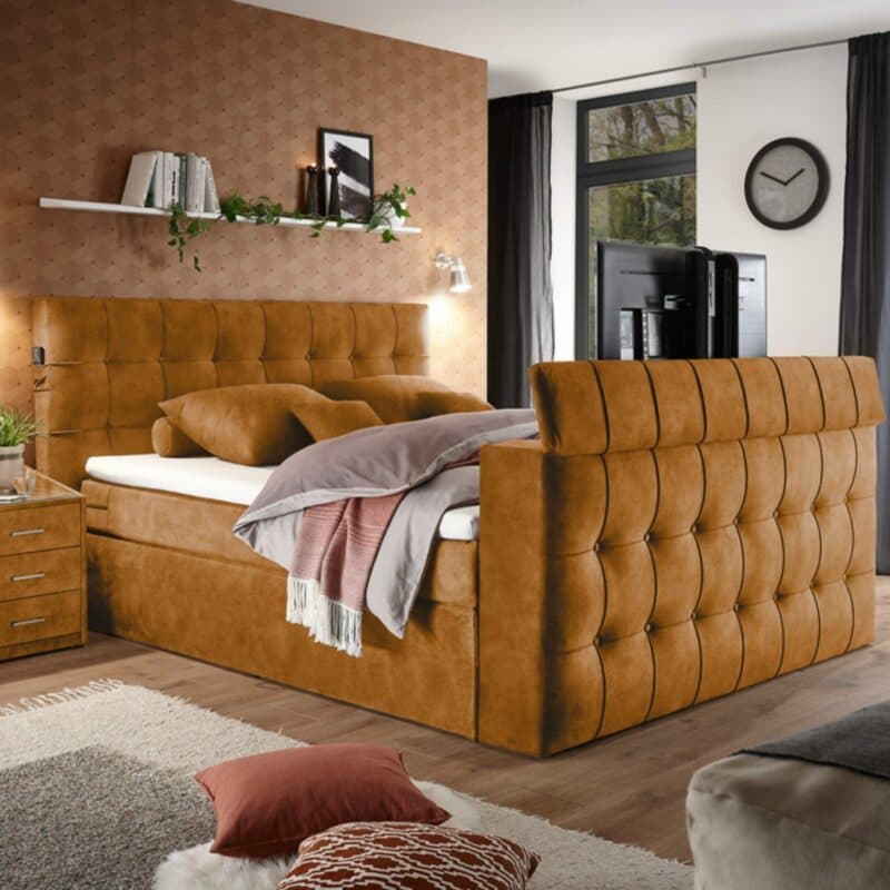 set one by Musterring richmond Boxspringbett 180 x 200 cm mit einem Microveloursbezug in Amber als Wohnbeispiel mit ausgefahrener TV-Halterung